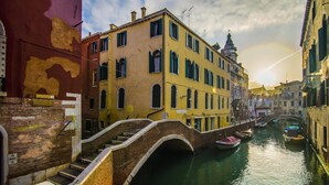 A canal with a bridge, colorful buildings, and a clear sky. - B&B Le Marie (Venice)