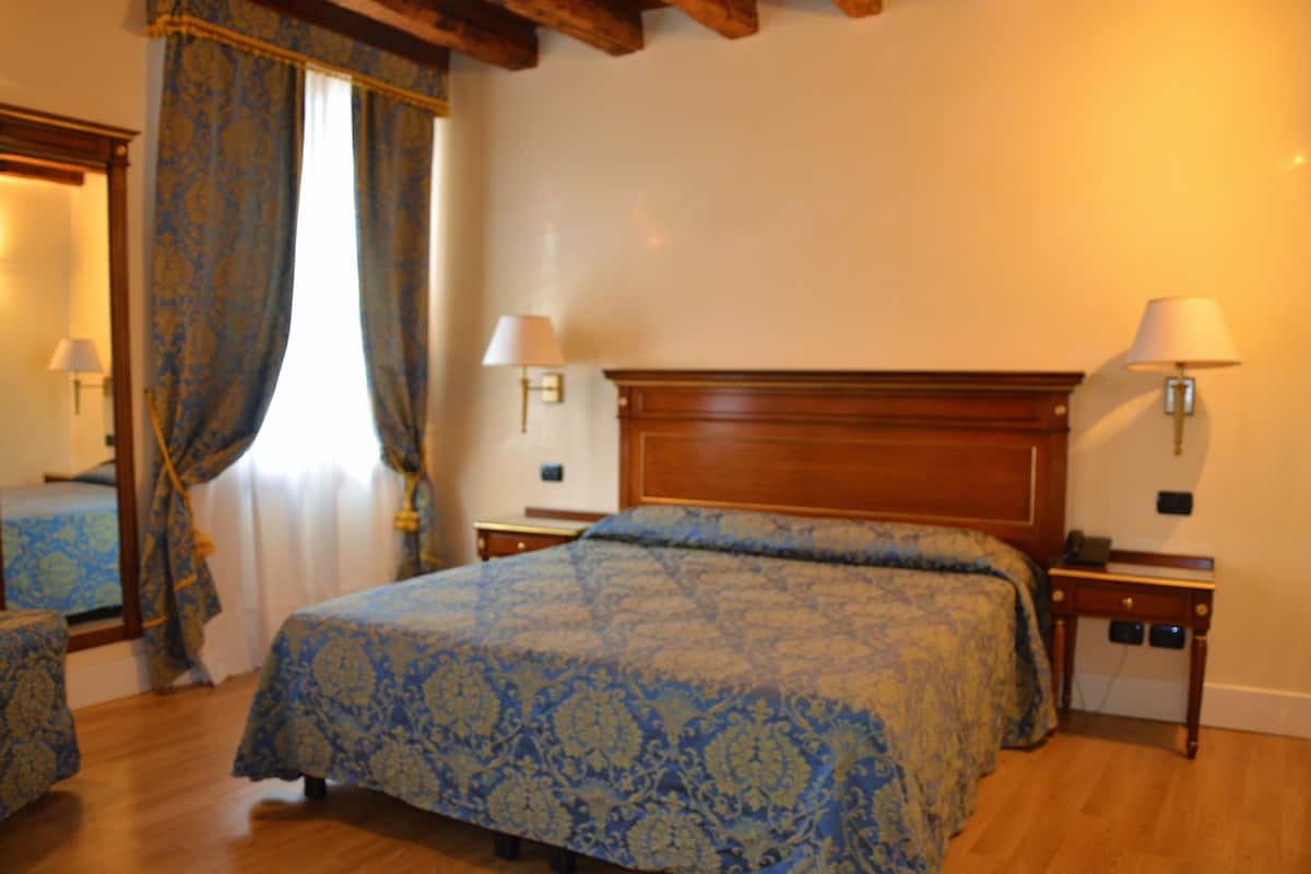 Un dormitorio con una cama grande, dos mesitas de noche con lámparas, un cabecero de madera y una ventana con cortinas.