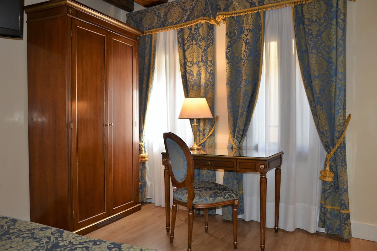 Una habitación con un armario de madera, un escritorio con silla y cortinas azules estampadas.