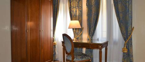 A room with a wooden wardrobe, a desk with a chair, and blue patterned curtains.