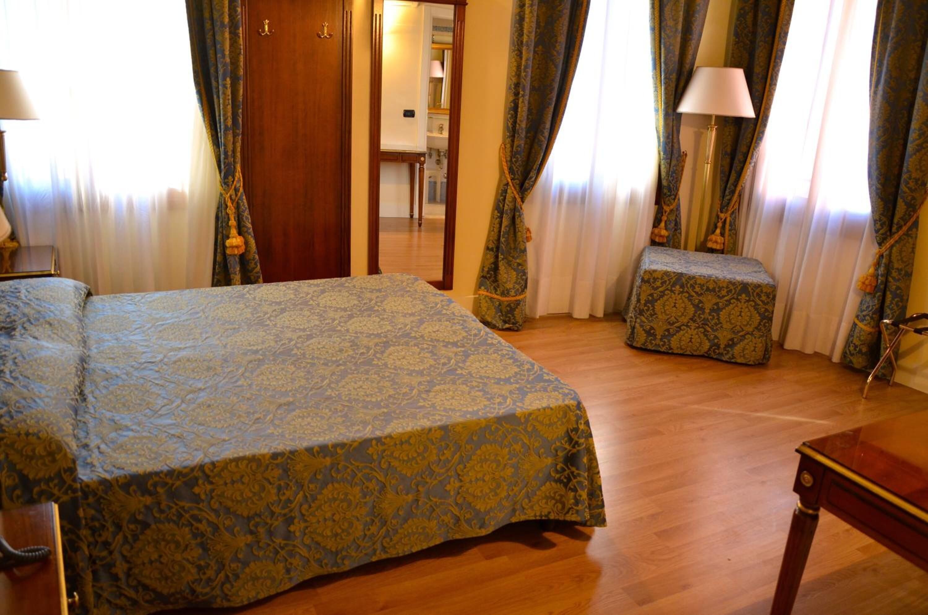 Ein Hotelzimmer mit einem großen Bett, einem Nachttisch, einer kleinen Bank und einer Lampe.