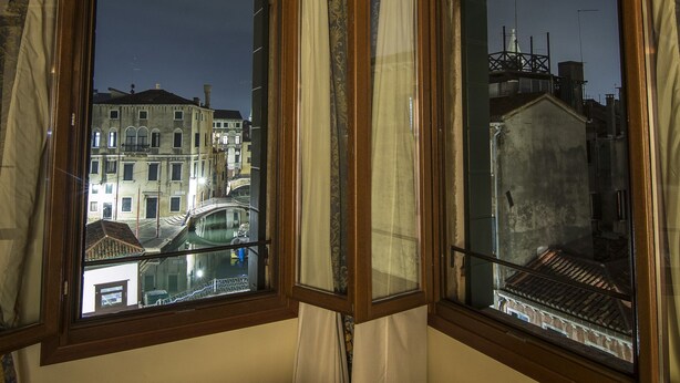 A room with a large window overlooking a cityscape at night, featuring a wooden ceiling and patterned curtains. - B&B Le Marie (Venice)