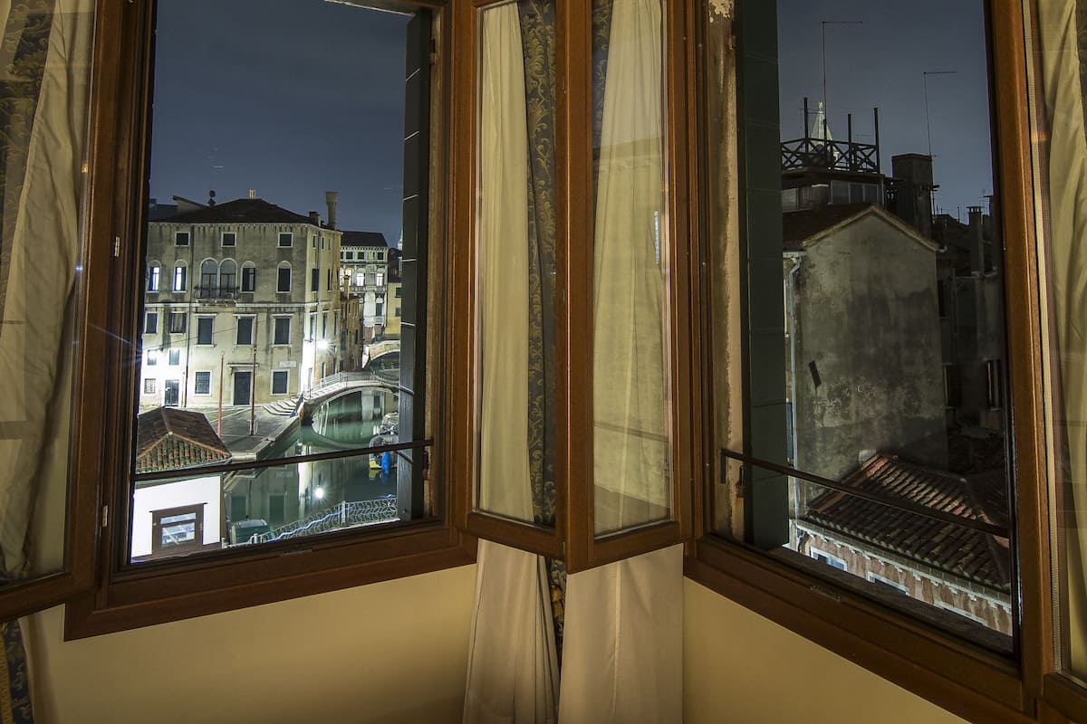Una habitación con un amplio ventanal que da a un paisaje urbano nocturno, con techo de madera y cortinas estampadas.