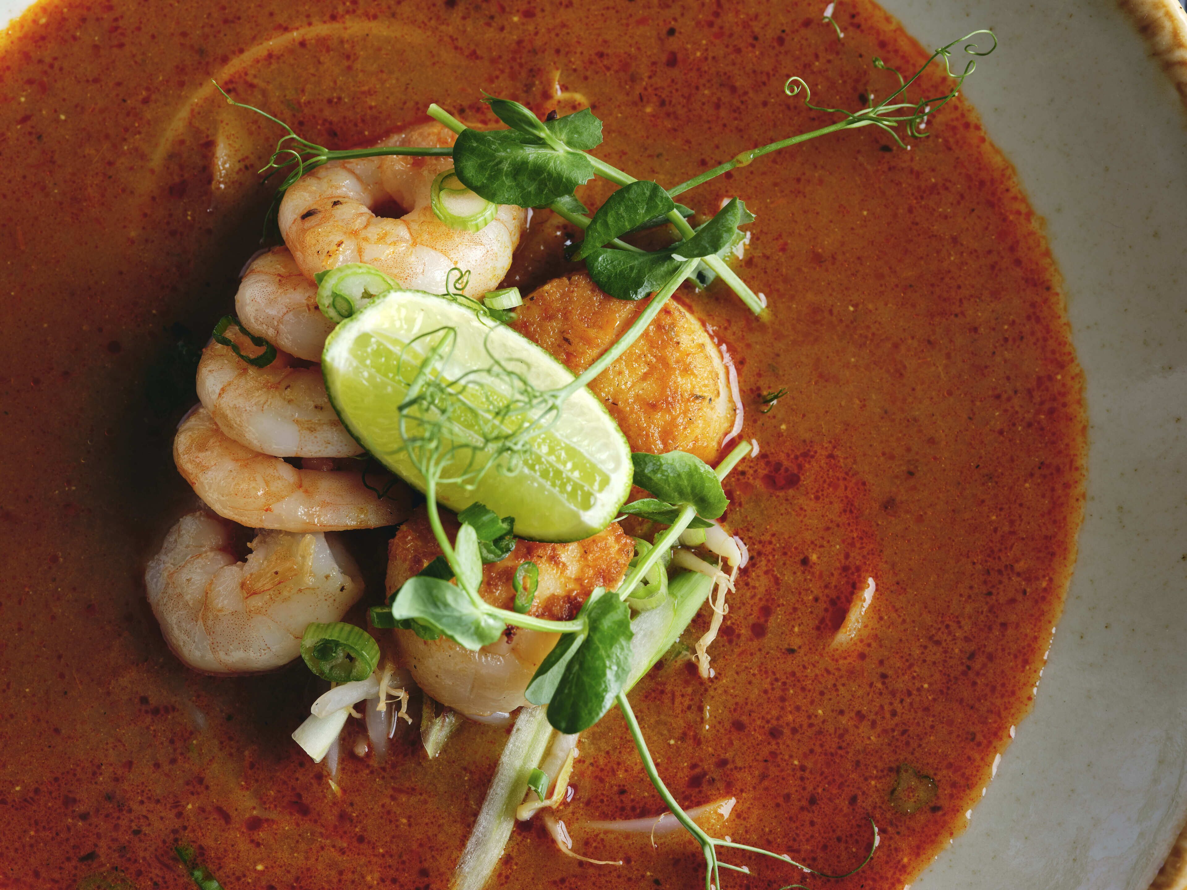 Un plato con camarones, lima y vegetales verdes.