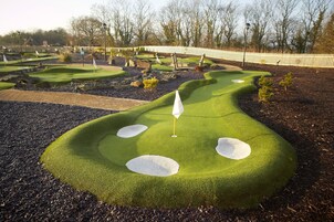 Un campo de mini golf con varios hoyos, una valla blanca y árboles al fondo.