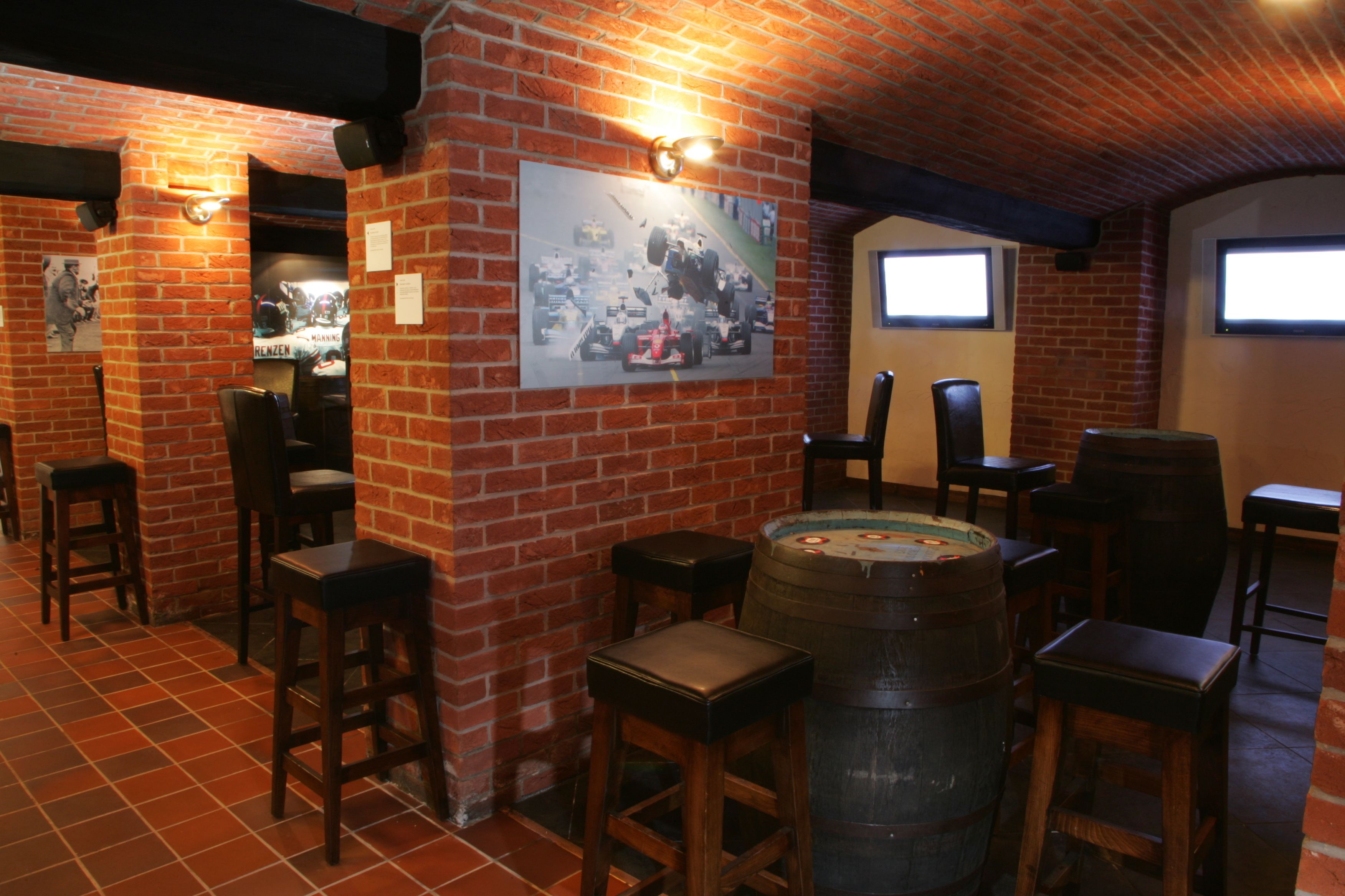 Un área de bar con paredes de ladrillo, taburetes de madera, un barril grande y un cartel en la pared.