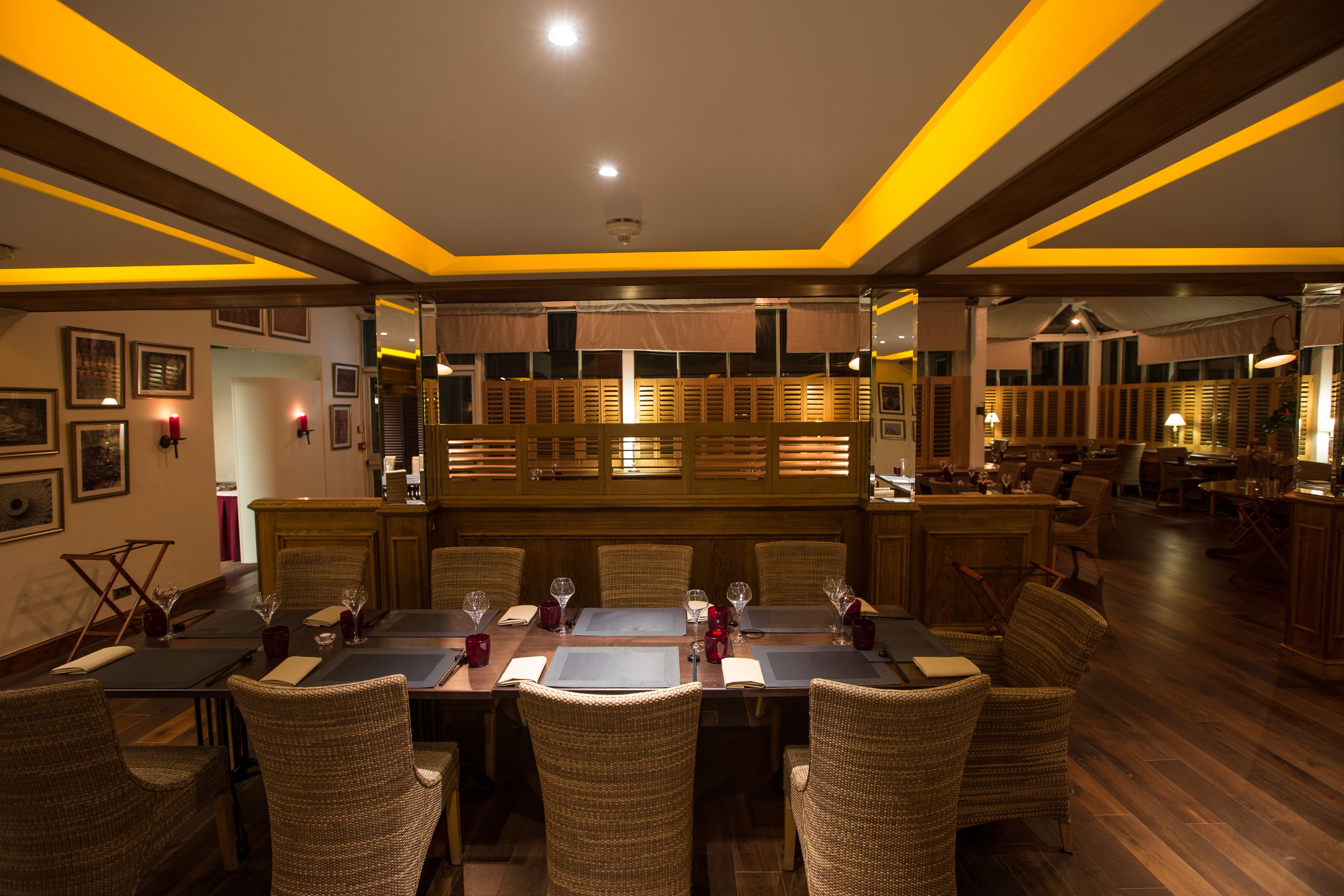 A restaurant with a long dining table, wicker chairs, and a bar area.