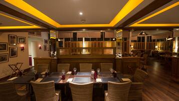 A restaurant with a long dining table, wicker chairs, and a bar area.