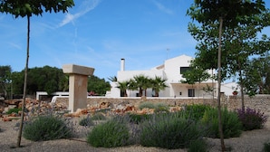 Un edificio moderno con un muro de piedra y fachada blanca, rodeado de un jardín ajardinado con diversas plantas y un sendero de grava.