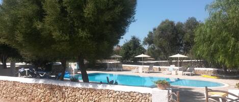 Una piscina al aire libre, sombrillas, sillones reclinables de piscina