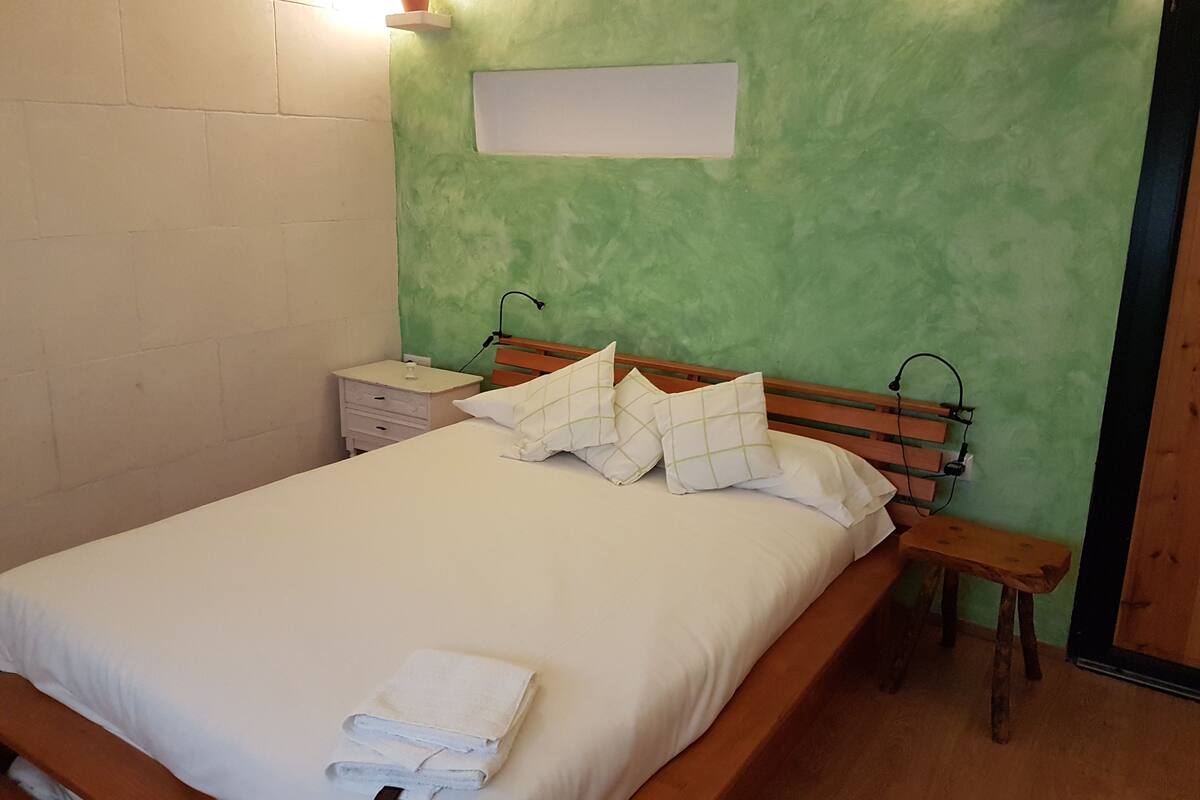 Une chambre à coucher avec un lit en bois, du linge de lit blanc, une table de chevet et une commode, ainsi qu’un mur vert.
