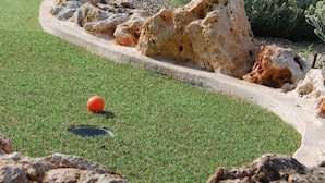 Un campo de golf con un pilar de piedra, un putting green y vegetación circundante.