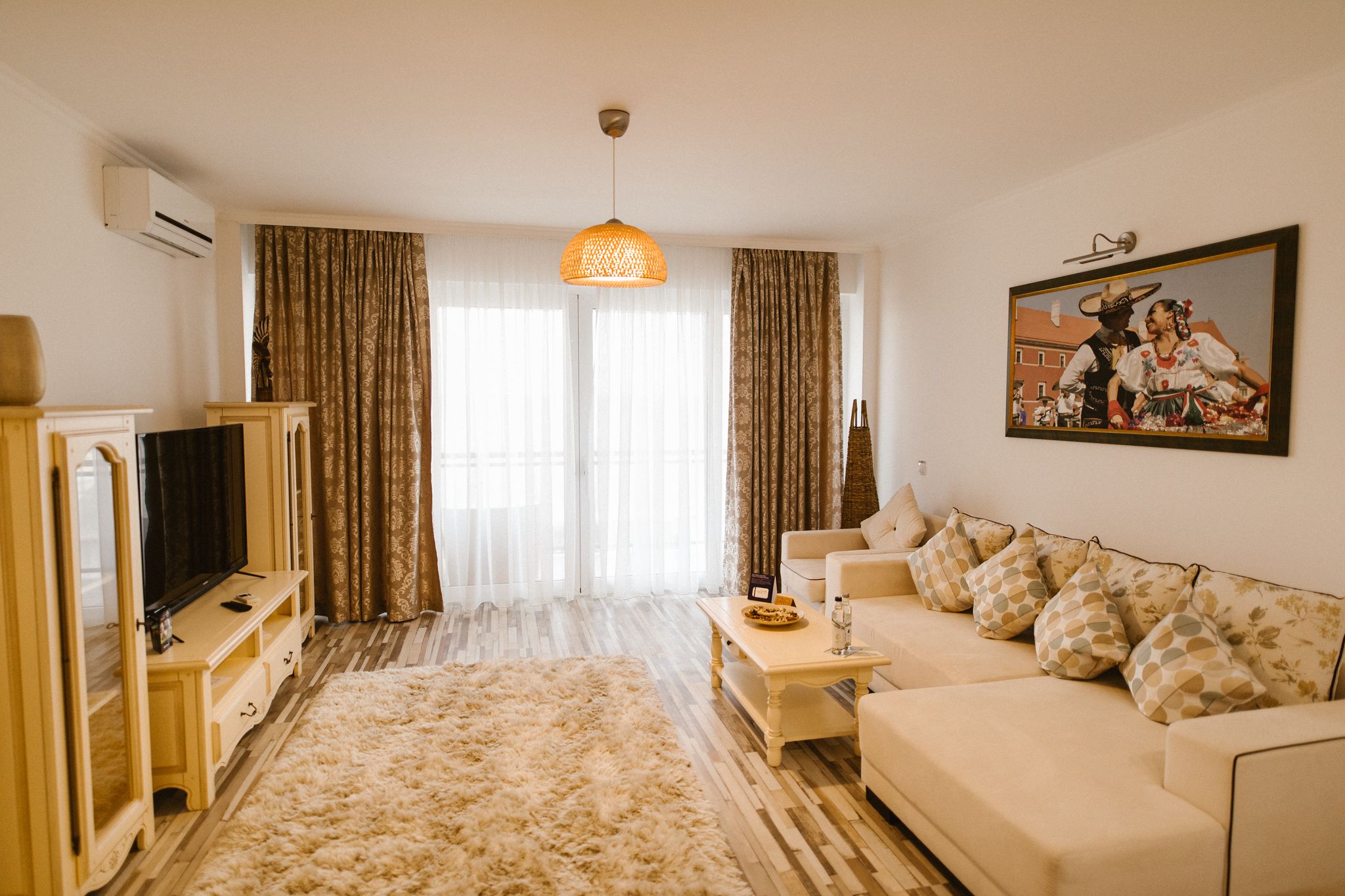 Una sala de estar con sofá, televisión, mesa de centro y un ventanal con cortinas.