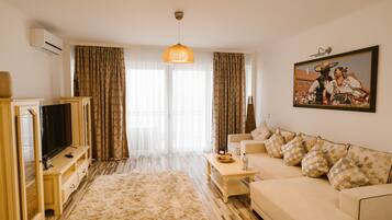 Una sala de estar con sofá, televisión, mesa de centro y un ventanal con cortinas.