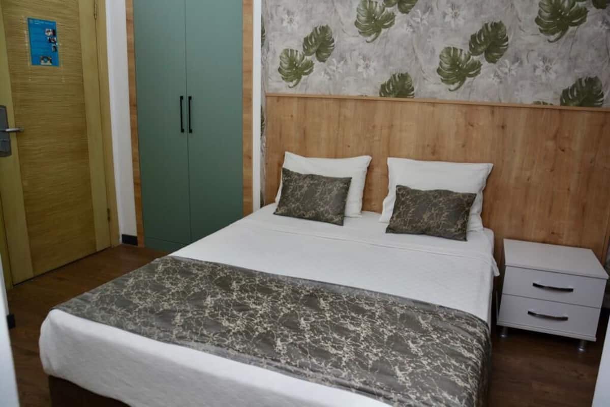 A bedroom with a bed, a nightstand, a wardrobe, and a wall with a leaf pattern.