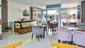 A modern cafe with a glass display case, comfortable seating, and a view of the street. - MySun Hotel (Izmir)