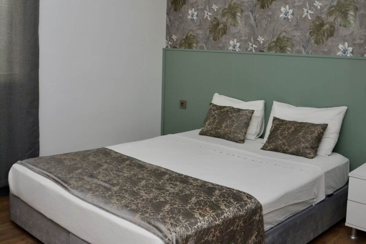 A modern bedroom with a large bed, a green headboard, and a floral-patterned wall.
