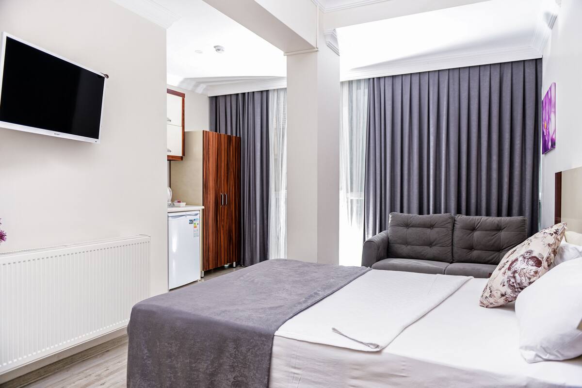 A modern hotel room with a bed, a TV mounted on the wall, a wardrobe, and a bathroom visible through a door.