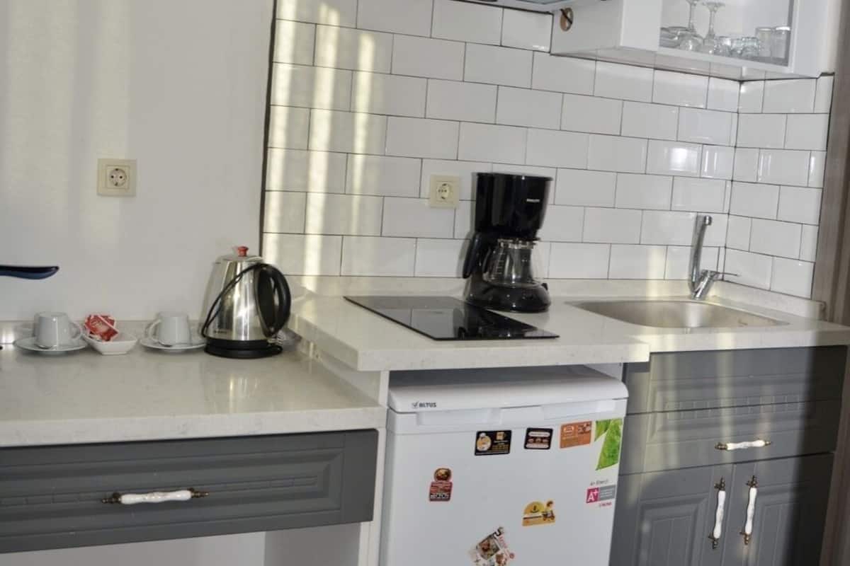 A compact kitchen with white cabinets, a built-in oven, a coffee maker, and a refrigerator with magnets.