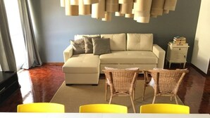 A living room with a sofa, two chairs, a small table, a lamp, and a nightstand with books. - Lemon Tree Apartments (Faro)