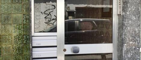 Una puerta de cristal con manija de metal, un pequeño escalón que lleva a ella, y una pared verde con diseño a la izquierda.