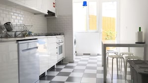A modern kitchen with white cabinetry, a black and white checkered floor, and a view of a wooden fence outside. - Lemon Tree Apartments (Faro)