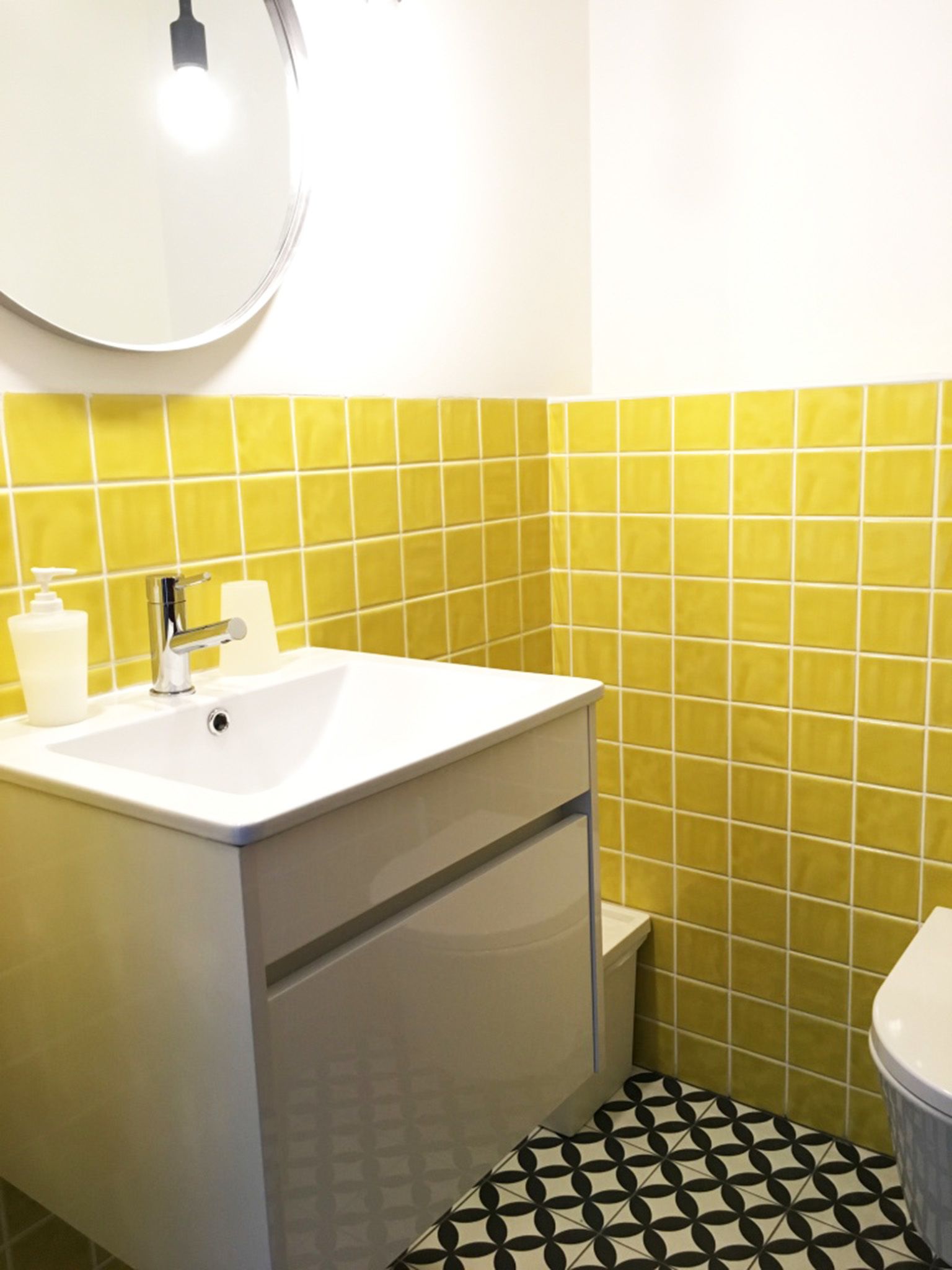 A bathroom with a white sink, yellow tiles, a black and white patterned floor, and a toilet.