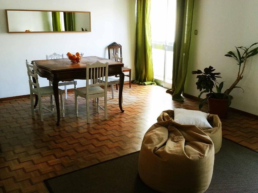 A dining area with a wooden table and chairs, a bean bag, a potted plant, and a large mirror on the wall.
