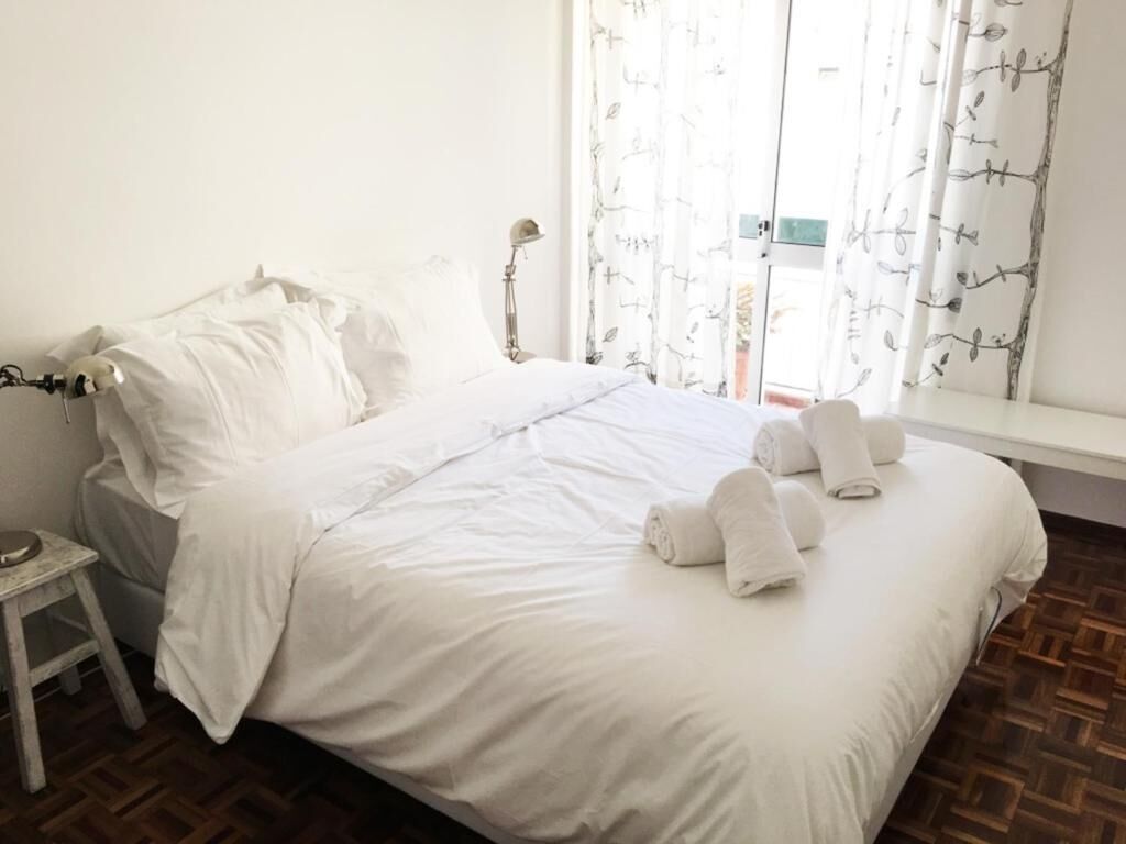 Una cama bien hecha con ropa de cama y toallas blancas, una mesita de noche y una ventana con cortinas estampadas.