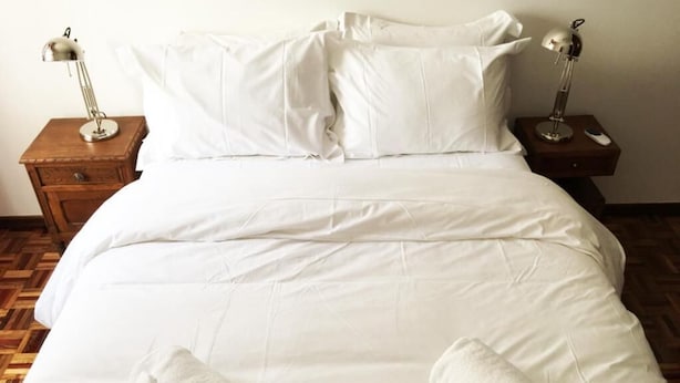 A neatly made bed with white linens, two bedside tables with lamps, and a wooden floor. - Lemon Tree Apartments (Faro)