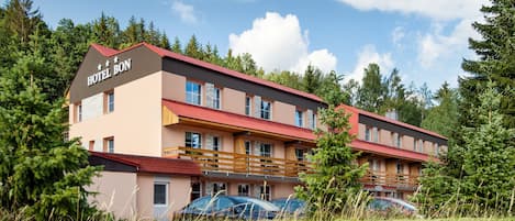 Un hotel de varios pisos con techo rojo y paredes color beige, rodeado de follaje.