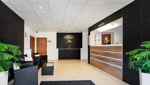 Zona de recepción de un hotel con mostrador de recepción, un reloj y un letrero que indica los servicios de restaurante, bolera y salón.