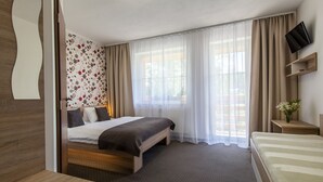 Habitación de hotel con cama, escritorio, televisor y ventana con cortinas.