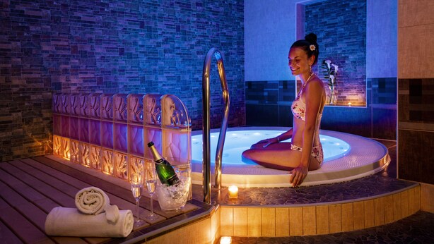 Zona de spa con hidromasaje, terraza de madera y una botella de champán.