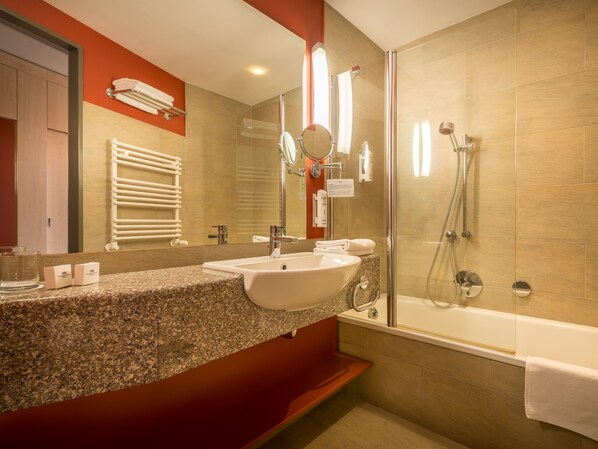 A modern bathroom with a granite countertop, a white sink, a glass-enclosed shower, and a large mirror.