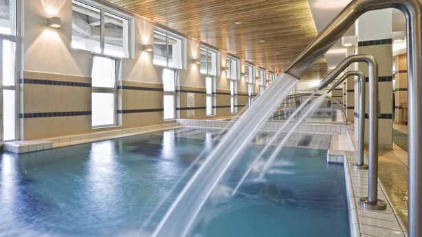 A swimming pool with a water feature, wooden ceiling, and tiled walls. - Ensana Bradet (Sovata)