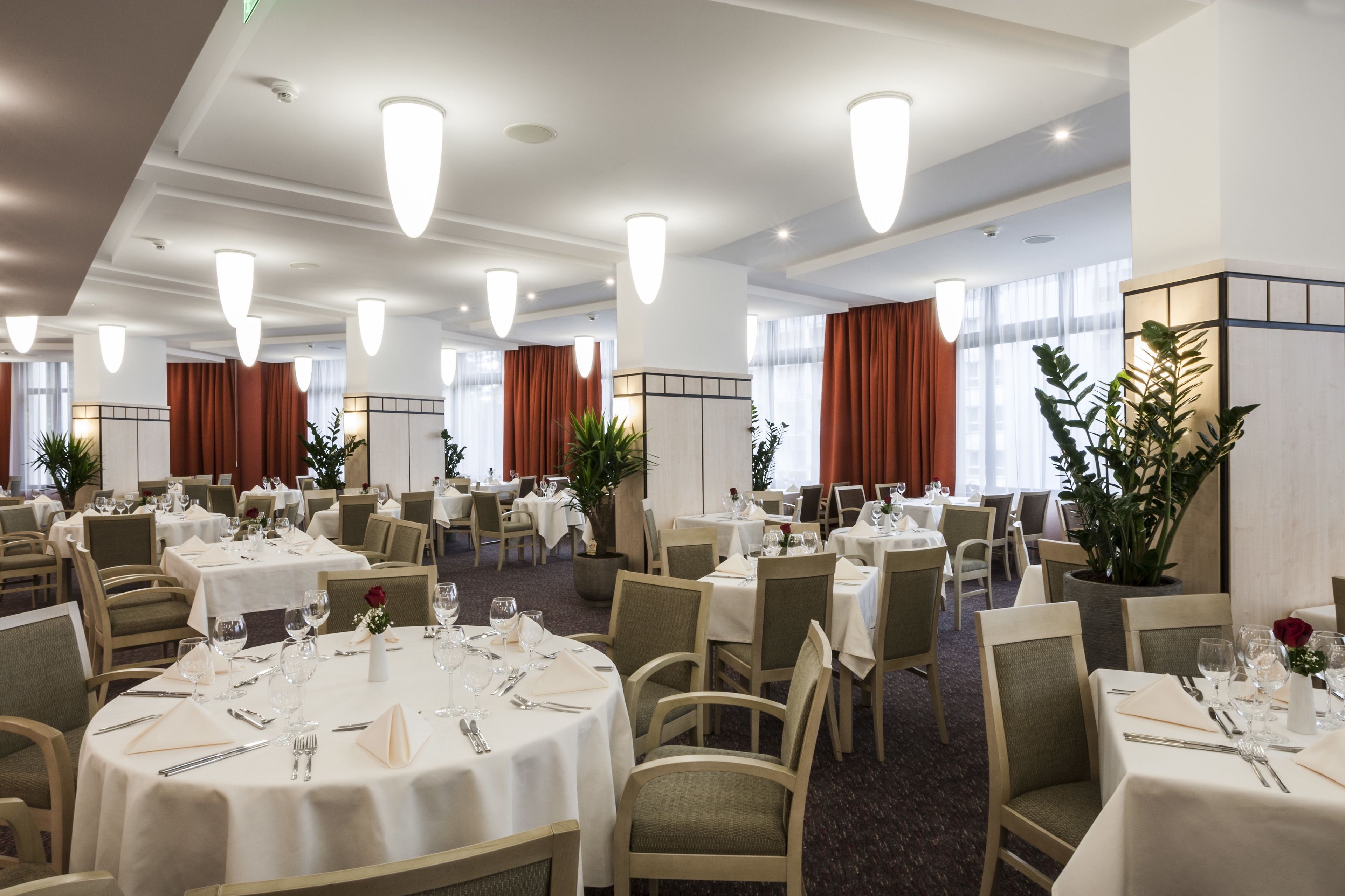 A hotel dining area with round tables, chairs, and pendant lighting.