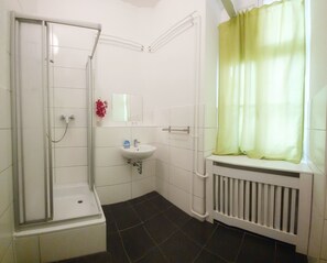 Une salle de bain avec une douche, un lavabo et une fenêtre avec un rideau.