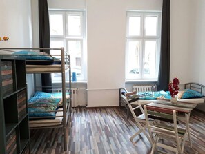 Une chambre avec des lits superposés, un plancher en bois, un radiateur et une fenêtre avec des rideaux.
