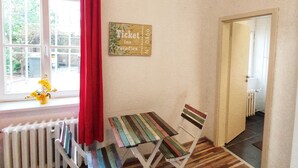 A room with a radiator, a window with a red curtain, a wooden table and chair, and a wall-mounted ticket sign.