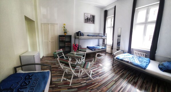 Une pièce avec des lits superposés, une petite table avec des chaises, un radiateur et une fenêtre avec des rideaux.