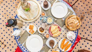 Desayuno dispuesto sobre una mesa con baldosas, con platos, tazas y diversas opciones de comida.