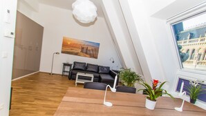 A modern living room with a wooden floor, a black sofa, a dining table with white candle holders, and a painting of a sunset. - Vienna Hotspot - Rathaus (Vienna)