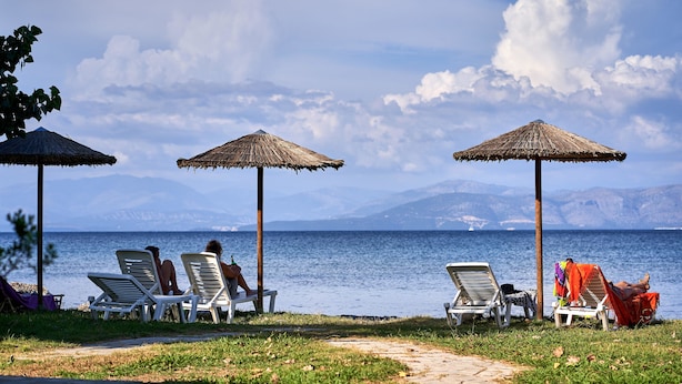 A beachside area with lounge chairs and thatched umbrellas, overlooking a calm sea and distant mountains. - Fardini Seaside Hotel (Corfu)