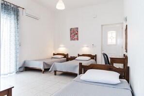 A room with two single beds, a wooden desk, a chair, a wall-mounted air conditioner, and a door with a window. - Fardini Seaside Hotel (Corfu)