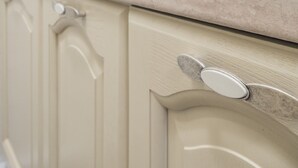 Una cocina con paredes de azulejos blancos, encimera color beige y grifo de acero inoxidable.