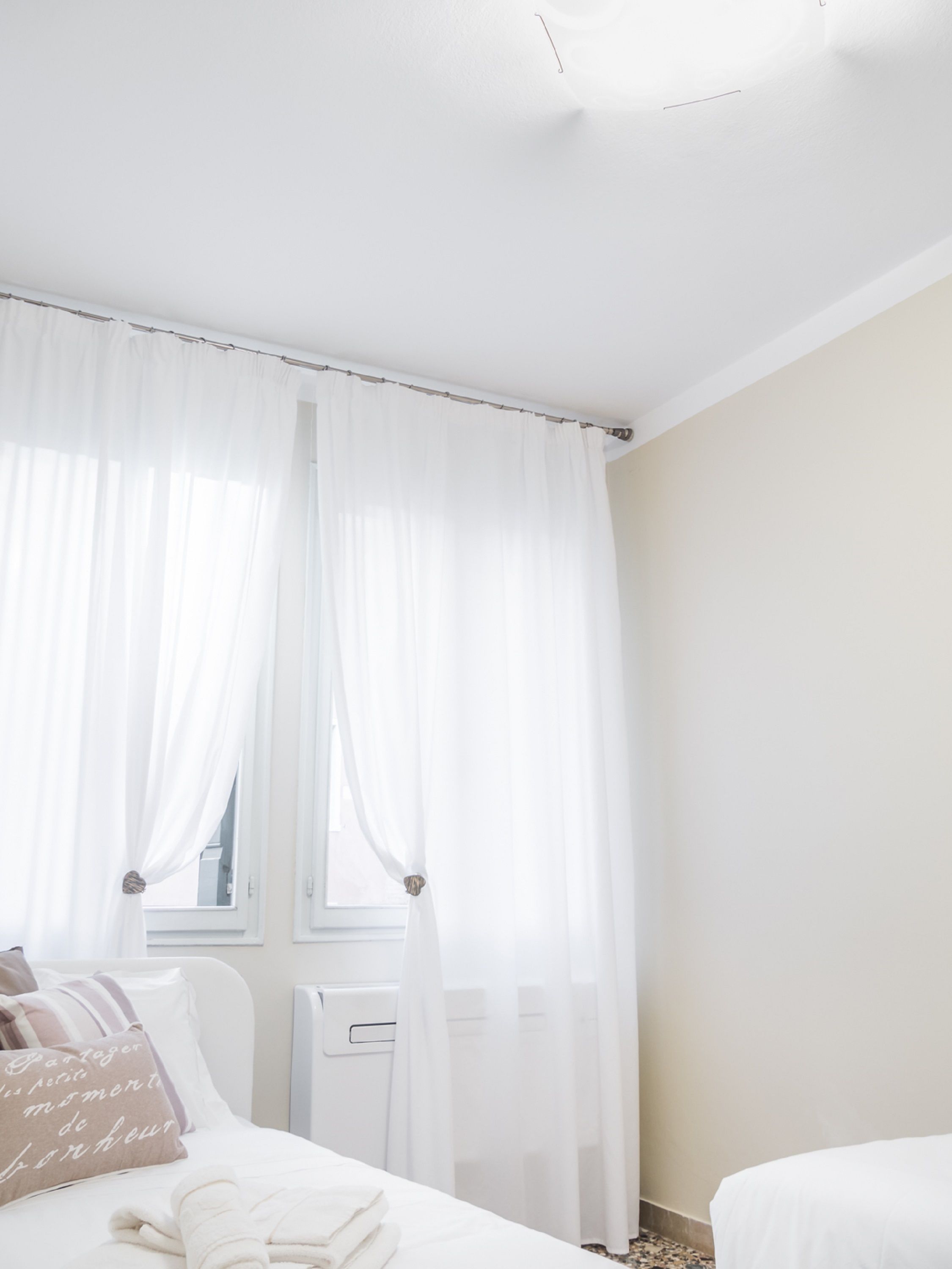 Ein Schlafzimmer mit einem Bett, einem Nachttisch, einer Heizung und transparenten weißen Vorhängen.