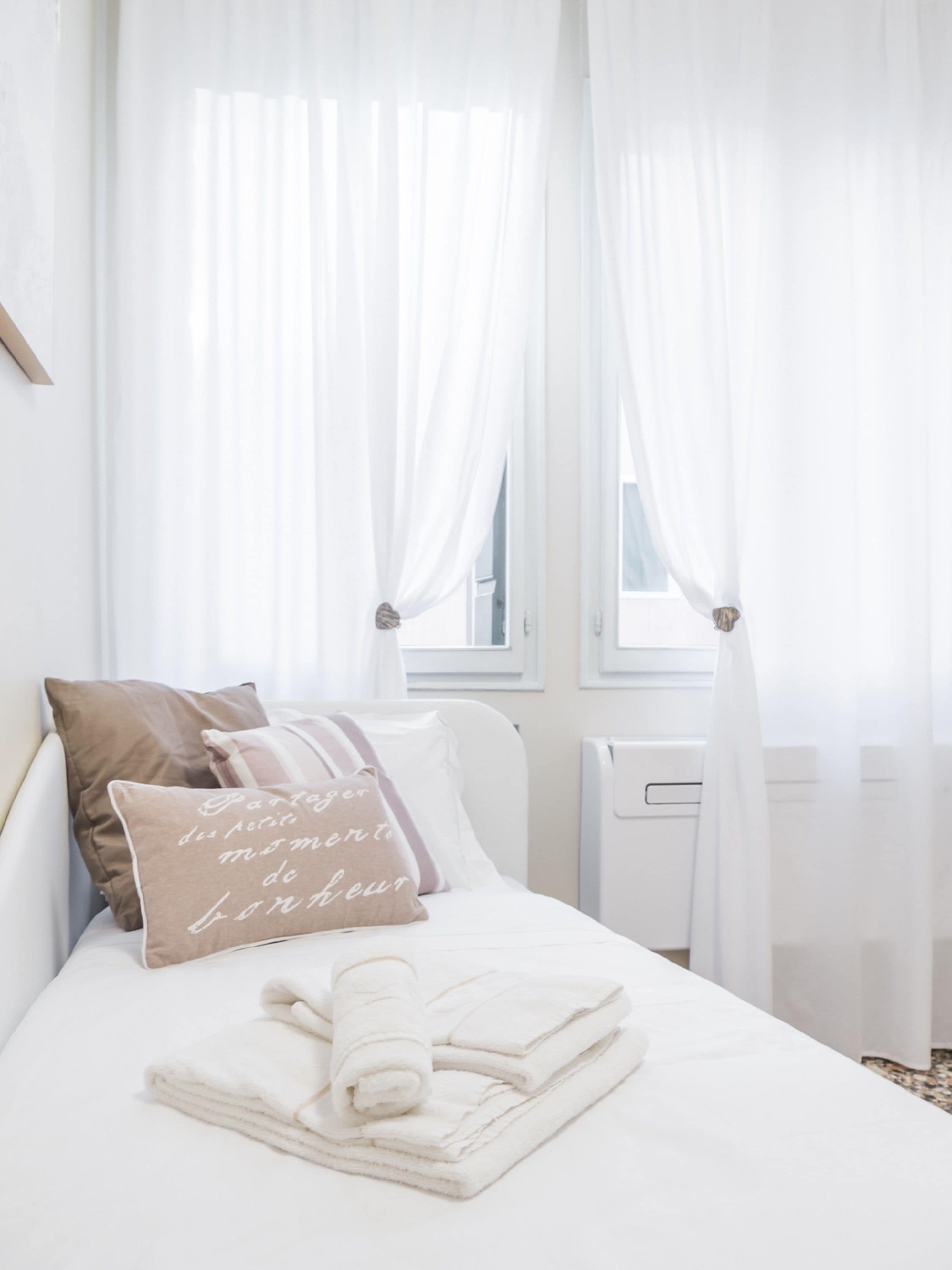 Un lit bien fait, avec des draps blancs, une serviette enroulée et deux oreillers ornés de motifs.