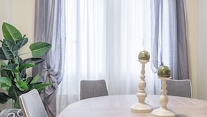Un comedor con una mesa redonda, dos candelabros, una planta en maceta y cortinas grises.