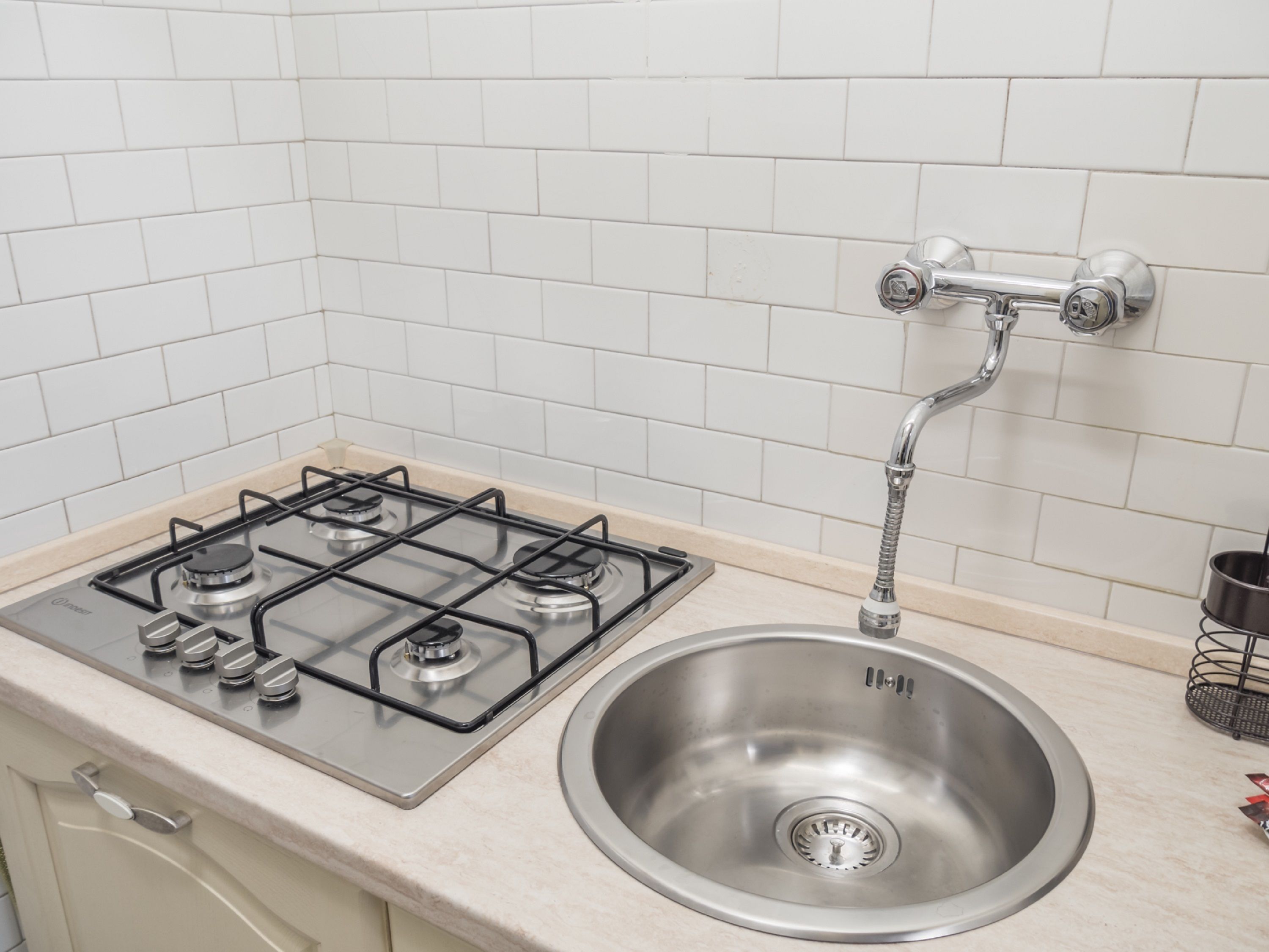 Una cocina con estufa a gas, pileta de acero inoxidable y salpicadero de azulejos blancos.